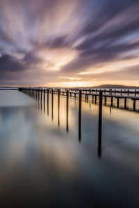 Wooden posts in sea against sky during sunset