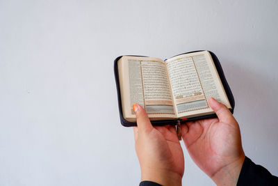 Close-up of hand holding book against white background