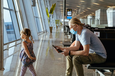 Man with girl ready to fly by airplane and the airport. father looking at smartphone in lounge on