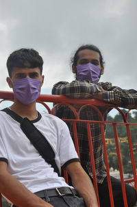 Two male friends with wearing face mask sitting outside with looking at camera 