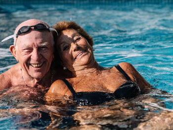 Cheerful senior couple smiling brightly while swimming together in outdoor pool during summer holidays