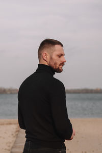 Young man looking at sea shore against sky