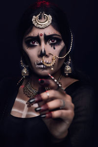 Close-up of young woman in traditional clothing with spooky make-up against black background