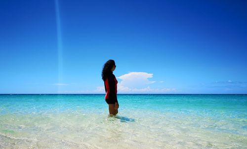 Woman standing in sea against blue sky