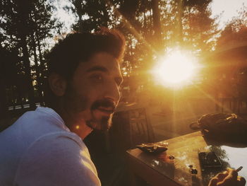 Close-up of man smoking at table against trees during sunset