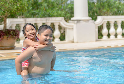 Portrait of boy carrying sister on back in swimming pool