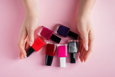 Female hands with bright nail polishes. a group of colored nail enamel on a pink background.