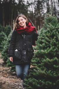 Portrait of smiling young woman standing in forest during winter
