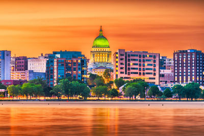 Buildings by river against sky during sunset