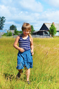 A boy in blue shorts and a striped t-shirt walks through the meadow. village houses in the back. 