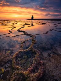 Man standing at frozen sea against sky during sunset