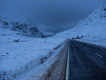 Road by snow covered mountain against sky