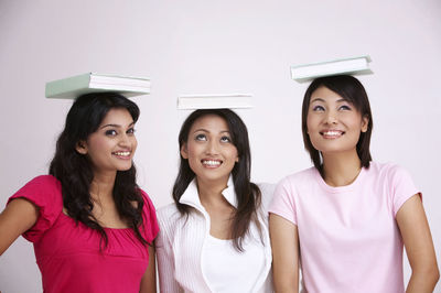 Smiling friends with books on heads against white background