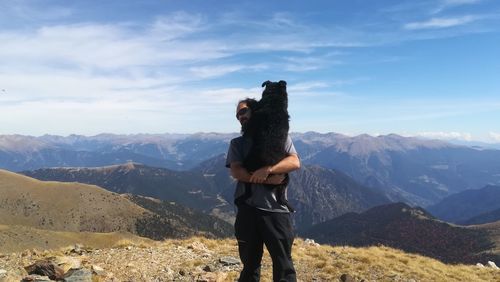 Man holding dog while standing against mountain