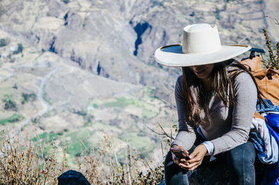 Woman using mobile phone while sitting on mountain