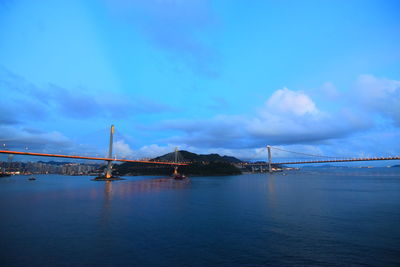 View of suspension bridge over sea against cloudy sky