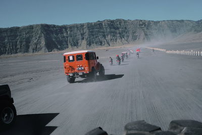 People on road by mountains against clear sky