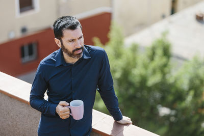 Relaxing moment of a middle-aged man standing on the balcony drinking coffee