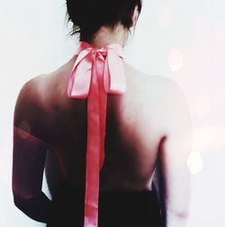 Rear view of shirtless woman wearing ribbon against white background