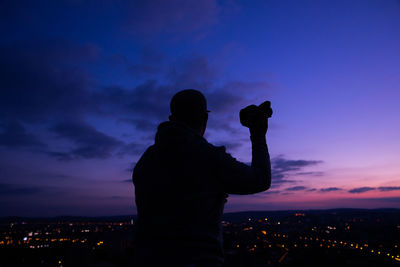 Silhouette man photographing cityscape against sky during sunset