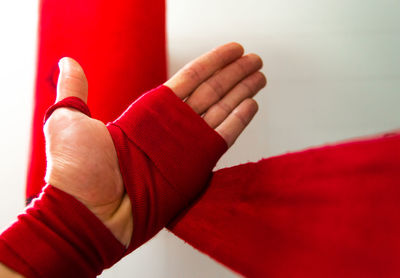 Cropped hand of person wrapping bandage against wall