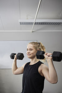 Smiling young beautiful woman leaning on gymnastics rings at health club