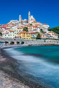 Buildings by sea against clear blue sky