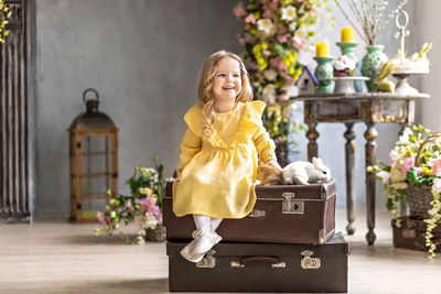 A blonde toddler girl in a yellow dress sits on old suitcases with  rabbits. emotions. easter