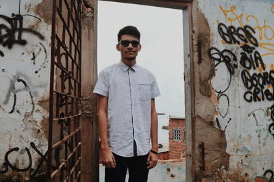 Portrait of man standing by old graffiti wall