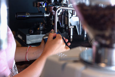 Midsection of barista holding cup by machine in cafe