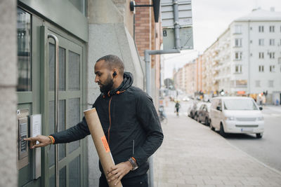 Male messenger holding package while ringing intercom of building