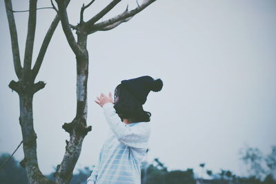 Low angle view of young woman standing against clear sky