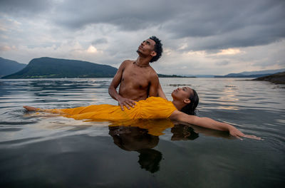 Full length of shirtless man in sea against sky