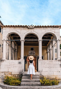 Young woman in white dress standing on stairs of an old building, town, street.