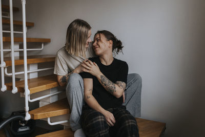 Smiling homosexual couple looking at each other while sitting on wooden stairs