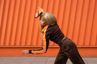 Cheerful african american woman in sportswear dancing in the street on an orange background