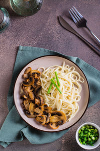 Udon noodles, fried champignons and greens on a plate on the table top and vertical view