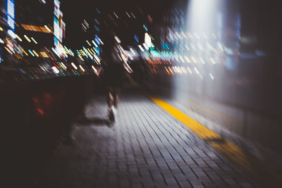 Blurred motion of people walking on illuminated street at night