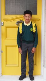 Portrait of smiling boy standing against yellow door