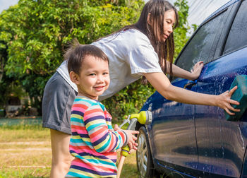 Full length of mother and son cleaning car outdoors