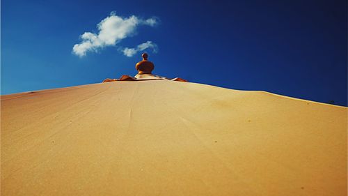 Low angle view of man sitting on sand against blue sky