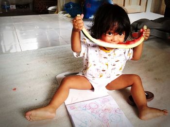 Portrait of cute girl eating watermelon while sitting at home