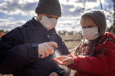 Father and daughter wearing respirator masks staying together on the empty bank of sea