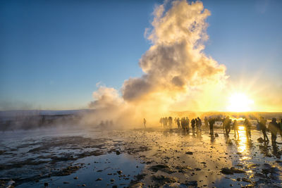 Panoramic view of people on shore against sky during sunset