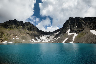 Rocky shore of a mountain lake with turquoise water in dense fog and high mountain in the background