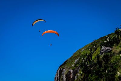 Low angle view of paragliding against clear blue sky