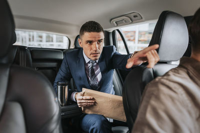 Businessman assisting driver while sitting in taxi