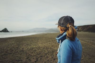 Rear view of woman standing at beach against sky