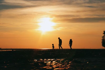 Silhouette people on beach against sky during sunset