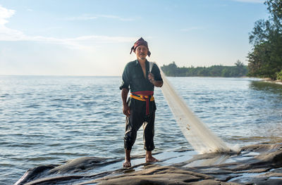 Portrait of fisherman standing by sea against sky